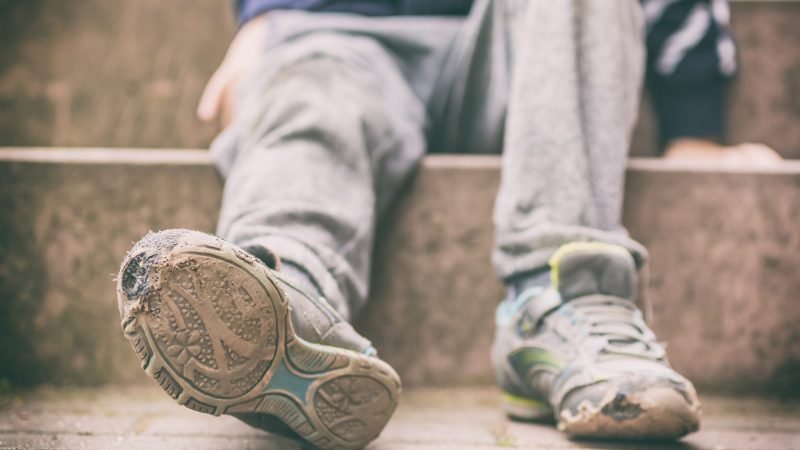 Alte kaputte Schuhe eines kleinen Jungen als Symbol für Kinderarmut Alte kaputte Schuhe eines kleinen Jungen als Symbol für Kinderarmut